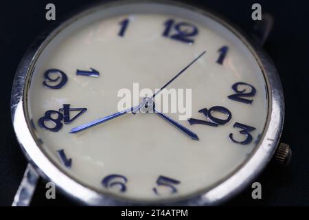 Le cadran d'une montre-bracelet avec des aiguilles bleues et des chiffres qui s'effritent. Macrophotographie. Concept du temps qui passe, vieillissement Banque D'Images