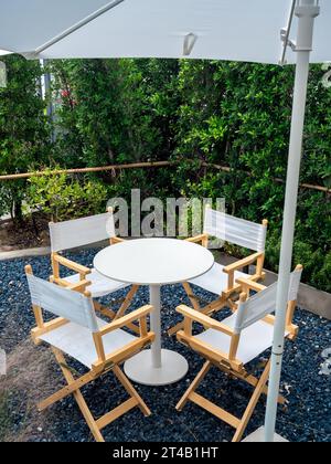 Quatre chaises de directeur vides, tissus et matériaux en bois avec table de forme ronde au jardin extérieur sur sol en pierre de gravier bleu dans la partie, style vertical. Banque D'Images