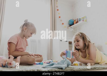 Enfants jouant avec des jouets colorés. Enfants assis sur la moquette dans la chambre à coucher ou la maternelle à la maison, la crèche. Jeu écologique éducatif pour enfant. Sœurs douces créatives concentrées d'âge préscolaire Banque D'Images