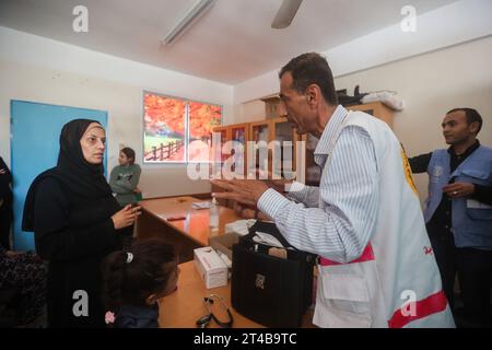 Le Dr Hassan Zein Al-DIN fournit des conseils médicaux à une palestinienne déplacée dans une école des Nations Unies pour soigner les personnes déplacées de la guerre dans le camp de Bureij, dans le centre de la bande de Gaza. Palestinien Dr Hassan Zein al-DIN, 54 ans, spécialiste de la médecine générale et des maladies chroniques. Il a été déplacé de la ville de Gaza vers la région de Bureij en raison de la guerre. Il se déplace à vélo entre les centres d’accueil pour soigner les déplacés et assurer le suivi de leurs cas au quotidien. Il se rend dans la ville de Gaza pour suivre les cas d’un certain nombre de patients dans les centres d’hébergement laissés par l’UNR Banque D'Images