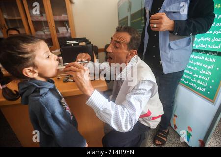 Le Dr Hassan Zein al-DIN traite une fille palestinienne déplacée dans une école des Nations Unies pour soigner des personnes déplacées de la guerre dans le camp de Bureij, dans le centre de la bande de Gaza. Palestinien Dr Hassan Zein al-DIN, 54 ans, spécialiste de la médecine générale et des maladies chroniques. Il a été déplacé de la ville de Gaza vers la région de Bureij en raison de la guerre. Il se déplace à vélo entre les centres d’accueil pour soigner les déplacés et assurer le suivi de leurs cas au quotidien. Il se rend dans la ville de Gaza pour suivre les cas d’un certain nombre de patients dans les centres d’hébergement laissés par l’administration de l’UNRWA. Soyez Banque D'Images