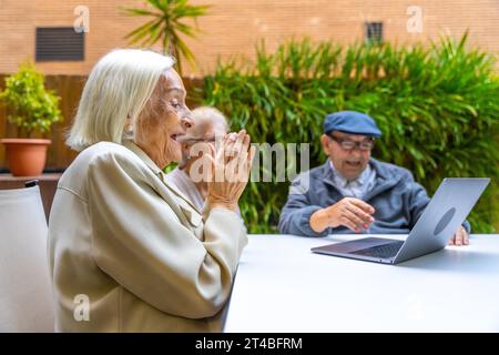 Les personnes âgées souriant et s'amusant en utilisant un ordinateur portable dans un gériatrique Banque D'Images