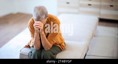 Anxiété et femme âgée pensant à un problème de santé mentale sur le canapé du salon dans la maison. Triste personne âgée avec dépression, stress à la maison et Banque D'Images