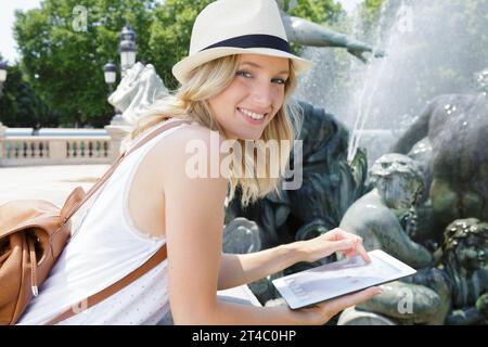 femme posant à côté de la fontaine en utilisant sa tablette Banque D'Images