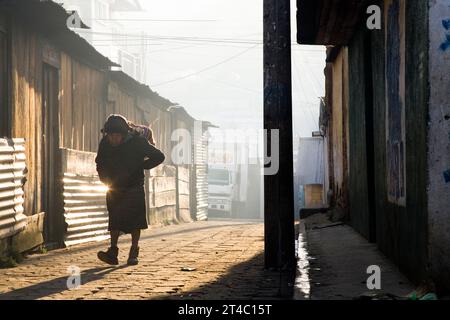 Un homme âgé porte une lourde meute le long d'un chemin de terre au lever du soleil à Nahuala, au Guatemala. Banque D'Images