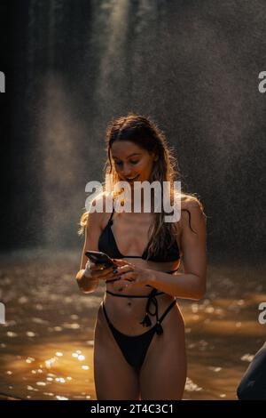 Femme touriste près d'une cascade prend une photo sur un smartphone. Banque D'Images