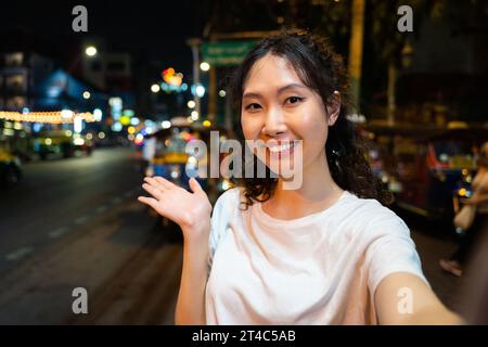 Portrait d'heureux voyageur hipster asiatique solitaire relaxant prenant une photo de selfie ou vlogging avec un sourire heureux dans la rue à Bangkok, Thaïlande. Touriste féminine explorant l'Asie du Sud-est. Banque D'Images