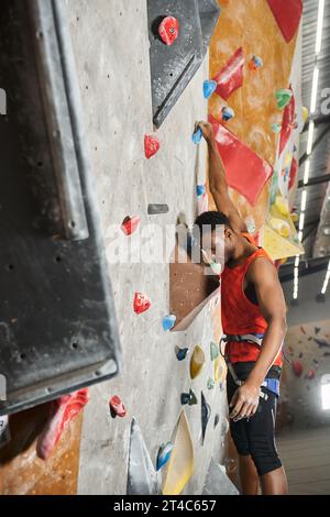 plan vertical d'un homme afro-américain accroché à ses doigts sur un mur rocheux et regardant vers le bas Banque D'Images