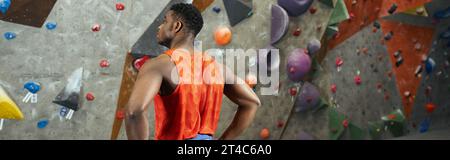 modèle masculin afro-américain athlétique debout à côté du mur de roche grimpant avec les mains sur les hanches, bannière Banque D'Images