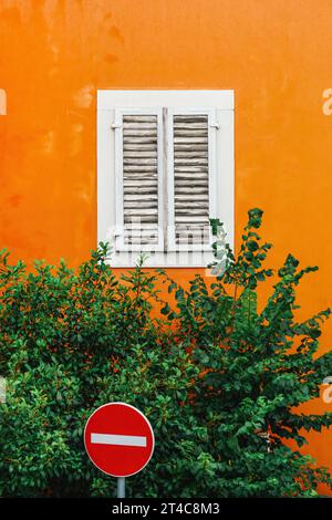 Scène de rue urbaine colorée - panneau de circulation interdit d'entrée à côté d'un vieux bâtiment orange avec fenêtre blanche fermée et cime d'arbre verte, mise au point sélective Banque D'Images