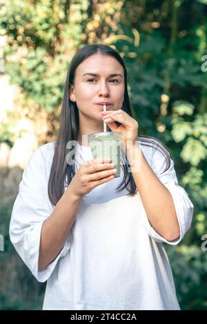 Femme élégante buvant du matcha latte dans le parc. Banque D'Images