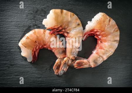 Trois crevettes tigrées géantes crues, nettoyées, sans tête et prêtes à cuire sur une assiette en ardoise sombre, vue de dessus, foyer sélectionné Banque D'Images