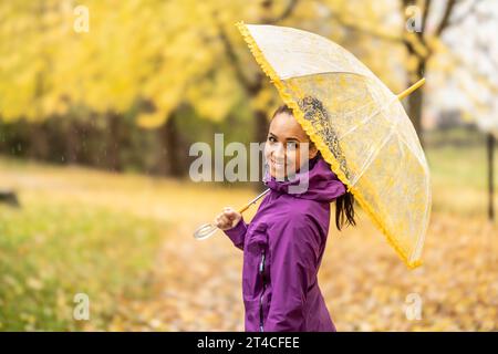 Portrait d'une jeune femme souriante sous un parapluie lors d'une promenade dans le parc d'automne. Banque D'Images