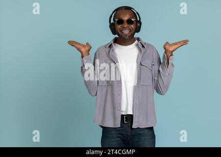 Le gars insouciant écoute de la musique un casque stéréo moderne présentant l'espace de copie sur les deux paumes Banque D'Images