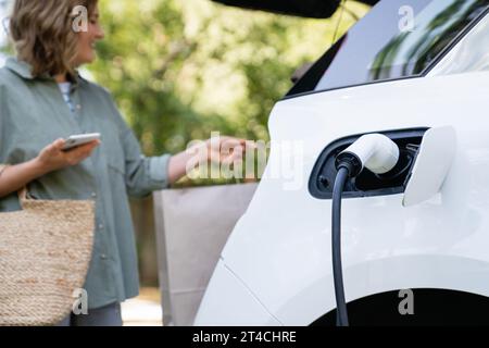 Femme prend un sac à provisions d'un coffre de voiture électrique de charge. Banque D'Images