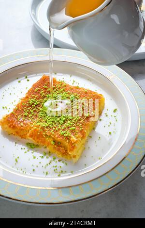 Morceaux de bonbons orientaux avec des pistaches dans une assiette blanche sur un sol blanc entouré d'ustensiles en argent et en cuivre Banque D'Images