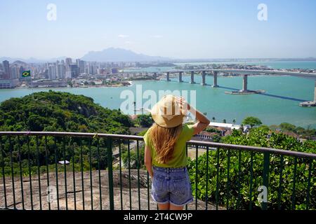 Vacances au Brésil. Vue arrière de la jeune femme voyageur appréciant le paysage urbain de Vitoria avec le pont Terceira Ponte, Vitoria, Espirito Santo, Brésil. Banque D'Images