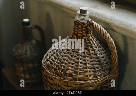 Bouteilles de vin vintage en osier près de la fenêtre. Mise au point sélective. Banque D'Images