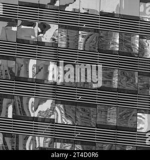 Une captivante capture en noir et blanc mettant en valeur les reflets de la ville déformés et juxtaposés dans les lignes structurées de la façade d'un bâtiment moderne Banque D'Images