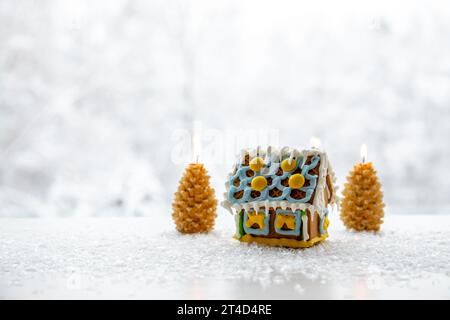 Bougies en forme d'arbre d'épicéa brûlant sur fond enneigé blanc avec paysage d'hiver avec maison mignonne en pain d'épice. Beaucoup d'espace de copie. Hiver et Noël Banque D'Images
