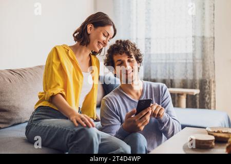 Portrait de jeune couple heureux qui regarde smartphone à la maison. Banque D'Images