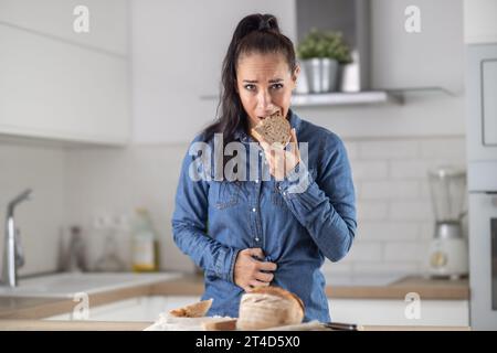 La femme ne peut pas manger du pain et des produits céréaliers à cause de l'intolérance au gluten. Une jeune femme cœliaque souffre de douleurs abdominales après avoir mangé du pain frais. Banque D'Images