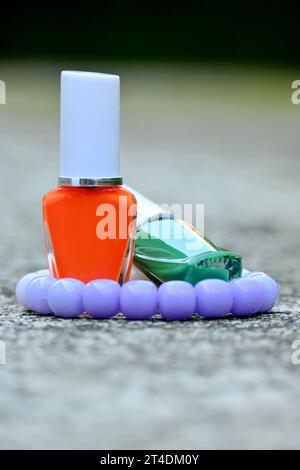 gros plan la paire de vert, orange blanc couleur bouteille en verre de peinture à ongles avec bracelet violet blanc soft focus fond brun gris naturel. Banque D'Images