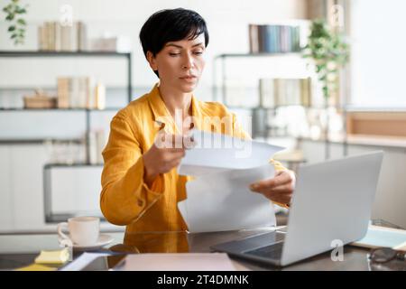 Femme entrepreneure d'âge moyen focalisée examinant des documents à l'espace de travail du bureau Banque D'Images