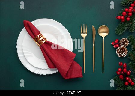 Assiette propre, couverts dorés. Table de fête avec décorations de noël. Célébration veille de Noël : arrangement plat. Rouge, accents dorés. Cônes de sapin allumés Banque D'Images