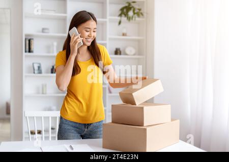 Concept de petite entreprise. Jeune femme asiatique emballant des commandes et parlant sur téléphone portable Banque D'Images