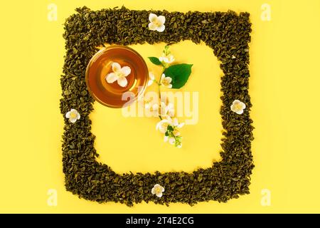 Maquette de feuilles de thé séchées et fleurs fraîches de jasmin en forme d'horloge carrée cadre avec tasse de thé au centre et branches de jasmin pointent à cinq heures iso Banque D'Images