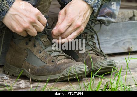 les mains de l'homme attachent les lacets sur ses bottes de randonnée sur les marches en bois Banque D'Images