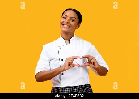 J'adore cuisiner. Heureuse femme chef noir tenant moule à biscuits en forme de cœur près de la poitrine Banque D'Images