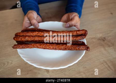 La femme tient de la nourriture dans sa main. La fille tient des saucisses kabanos sur une assiette. Tenant les saucisses en main. Banque D'Images