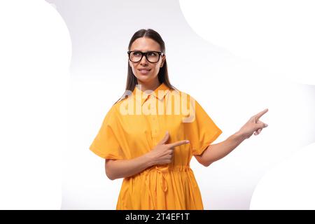 jeune femme aux cheveux noirs avec des lunettes vêtue d'une robe d'été orange montre un geste de classe Banque D'Images