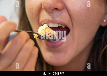 La femme mange de la nourriture. La femme mange du cheesecake. Plan rapproché d'une fille mangeant du gâteau. Visage en mangeant du gâteau. Banque D'Images