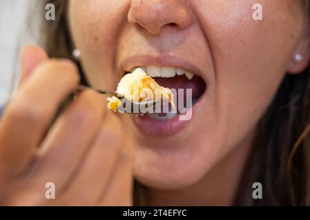 La femme mange de la nourriture. La femme mange du cheesecake. Plan rapproché d'une fille mangeant du gâteau. Visage en mangeant du gâteau. Banque D'Images