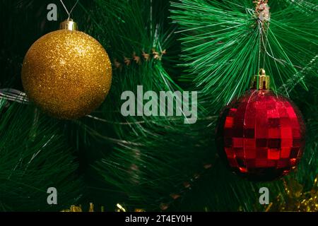 Deux jouets en forme de boule dorée et rouge accrochent sur les branches vertes d'un sapin de Noël artificiel Banque D'Images