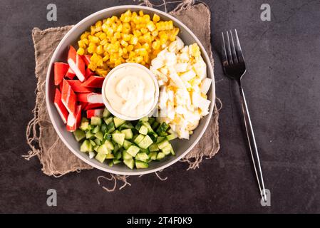 Salade de bâtonnets de crabe hachés avec maïs sucré, œufs, concombre et mayonnaise en pause dans le bol. Délices de fruits de mer. Banque D'Images