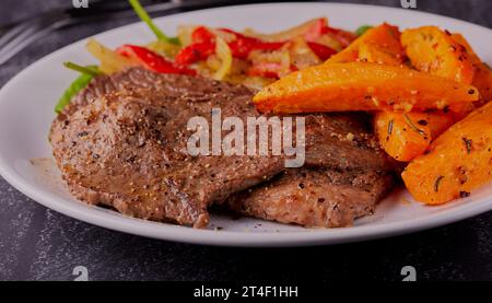 Steaks de bœuf finement coupés avec des quartiers de patates douces et une salade d'épinards. Banque D'Images