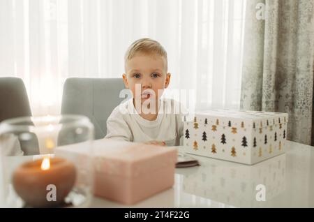 Un garçon prépare des cadeaux pour Noël. Cadeau sur la table. La bougie brûle. Banque D'Images