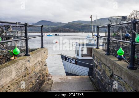 Un bateau de pêche vu amarré au bord de l'eau dans le port de Barmouth photographié le 22 octobre 2023 entre des pots empilés de homard et de crabe. Banque D'Images