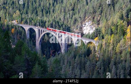 Davos Wiesen - octobre 2023 : un train de voyageurs rouge traverse le célèbre viaduc de Wiesener sur la ligne Davos - Filisur, le plus haut viaduc de s. Banque D'Images