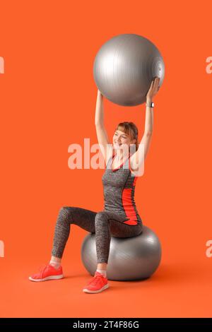 Jeune femme sportive avec des balles de fitness sur fond rouge Banque D'Images