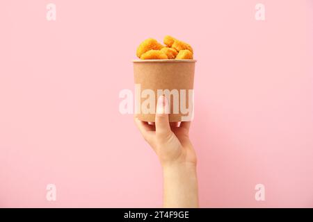 Femme tenant un seau en papier avec des pépites savoureuses sur fond rose Banque D'Images