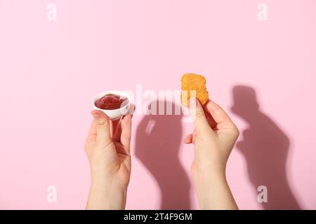 Femme tenant pépite savoureuse et bol de ketchup sur fond rose Banque D'Images