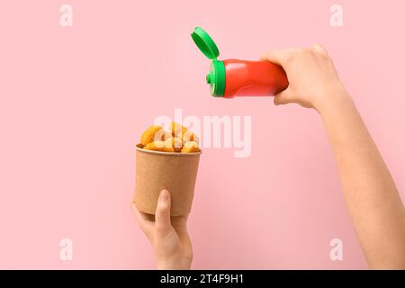 Femme tenant un seau en papier avec des pépites savoureuses et du ketchup sur fond rose Banque D'Images