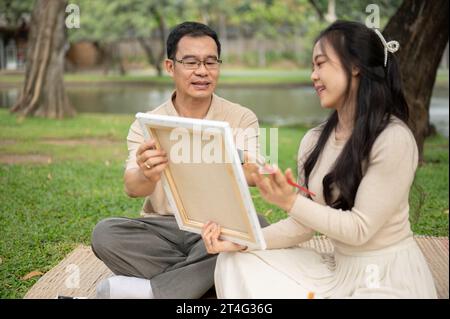 Une fille asiatique charmante et joyeuse aime pique-niquer dans un parc verdoyant avec son père, passer du temps à créer et peindre une image sur une toile ensemble. HAP Banque D'Images