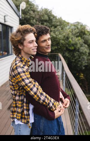 Heureux et diversifié couple masculin gay embrassant au balcon avec vue sur la forêt Banque D'Images