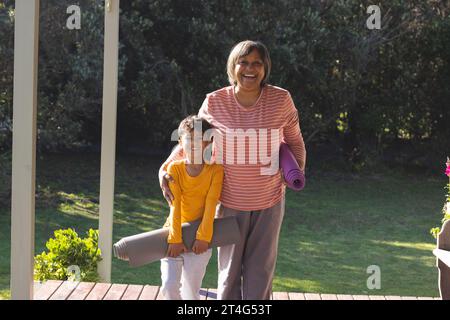 Portrait de grand-mère biracial heureux et petit-fils tenant des tapis de yoga dans le jardin Banque D'Images